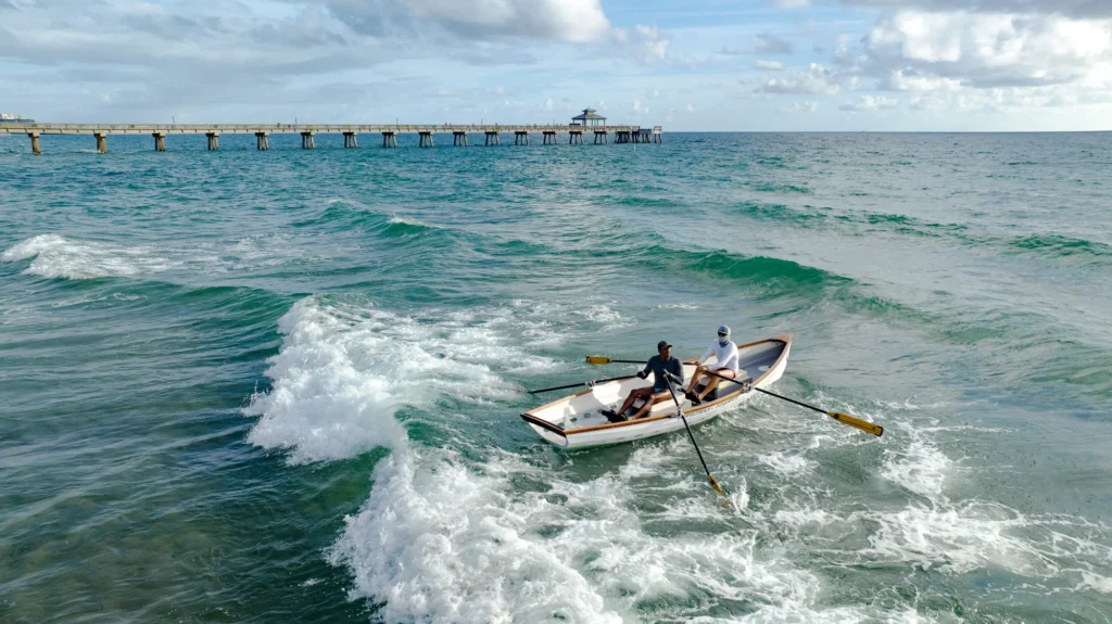 Small boat crossing waves beside a pier